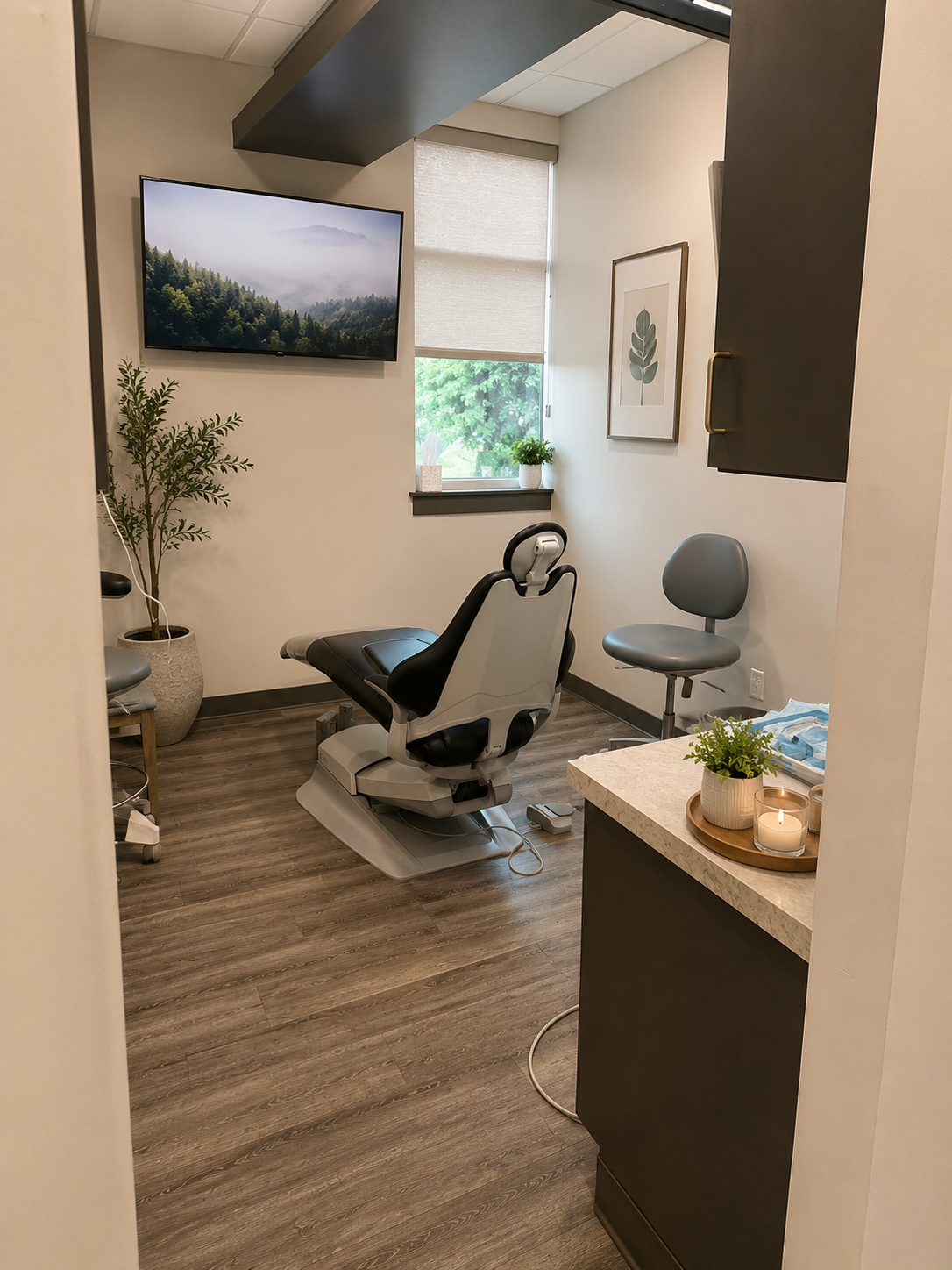 A calm treatment room with a nature scene on the wall-mounted screen, an olive tree and a lit candle on the counter