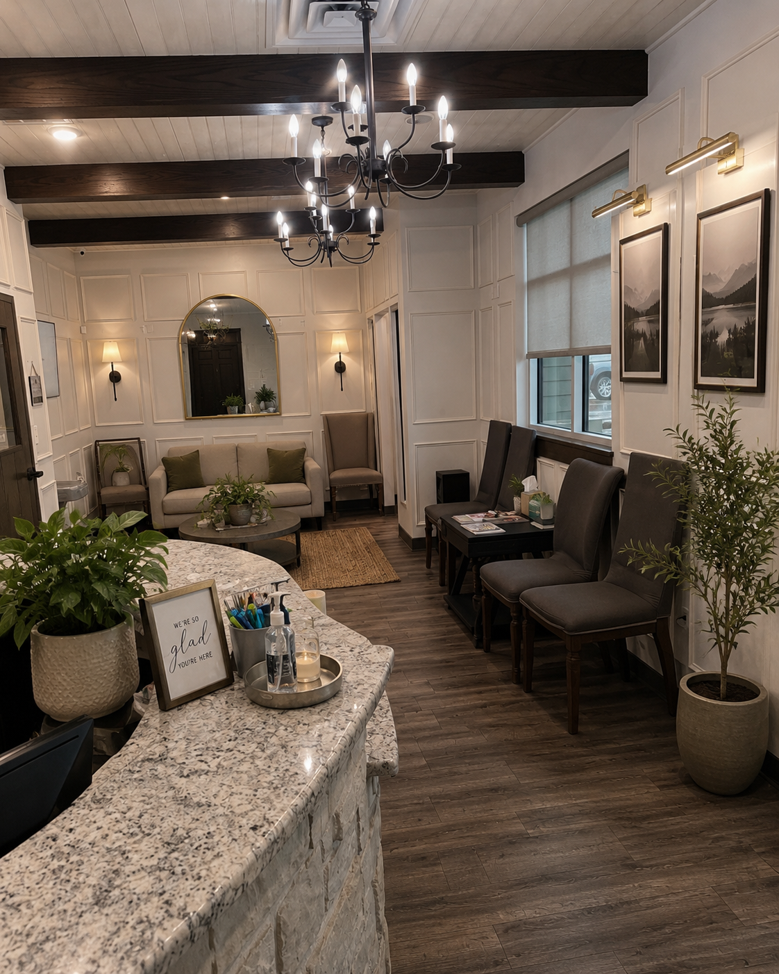 Warm, residential-style waiting room with a chandelier, wainscoting, an arched mirror and a "we're so glad you're here" sign
